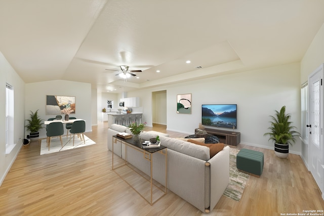 living room featuring light wood-type flooring, a tray ceiling, and ceiling fan