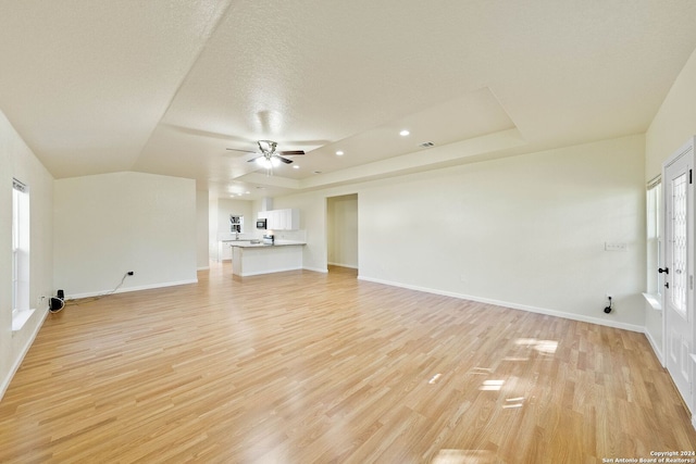 unfurnished living room with a tray ceiling, ceiling fan, light hardwood / wood-style floors, and a textured ceiling