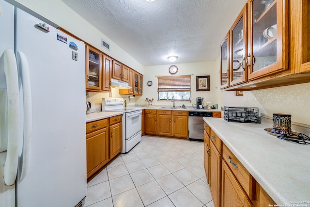 kitchen featuring a textured ceiling, white appliances, light tile patterned floors, and sink