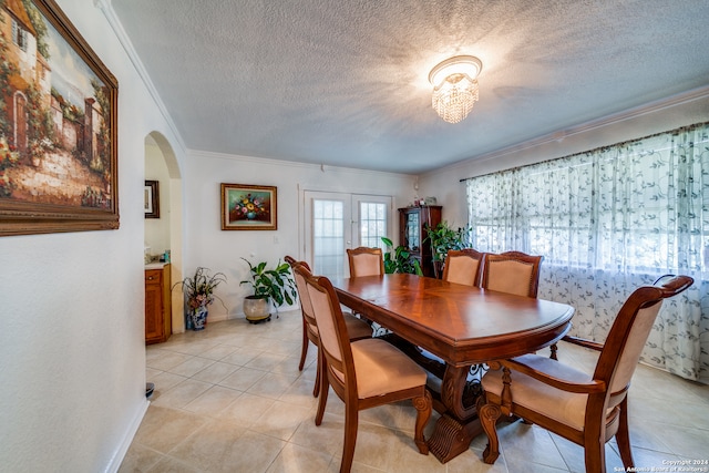 dining space with french doors, ornamental molding, a textured ceiling, light tile patterned floors, and a notable chandelier