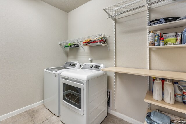 clothes washing area featuring separate washer and dryer, light tile patterned floors, and a textured ceiling