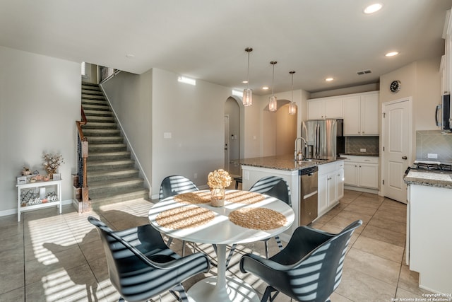 kitchen featuring appliances with stainless steel finishes, backsplash, a kitchen island with sink, dark stone countertops, and white cabinets