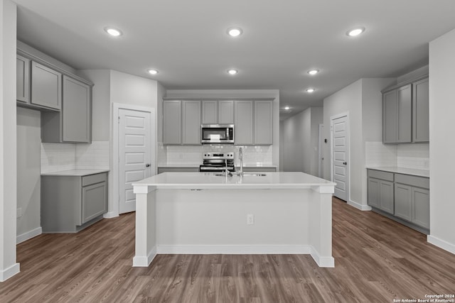 kitchen with gray cabinets, a center island with sink, and stainless steel appliances