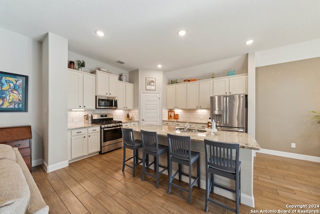 kitchen with a kitchen island with sink, light hardwood / wood-style flooring, white cabinets, and stainless steel appliances