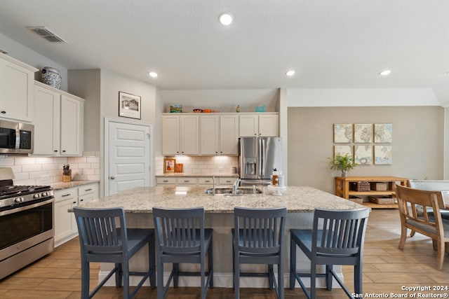 kitchen with white cabinets, appliances with stainless steel finishes, a center island with sink, and light stone countertops