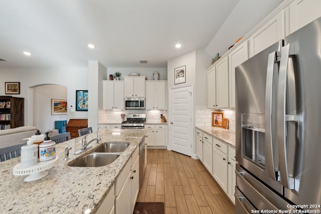 kitchen with light stone countertops, appliances with stainless steel finishes, light hardwood / wood-style flooring, and sink