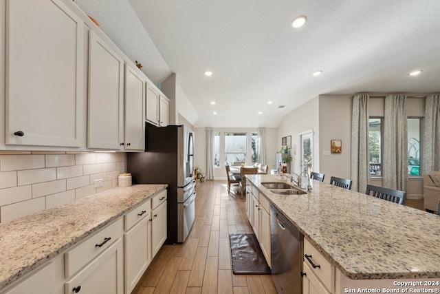 kitchen featuring light stone countertops, stainless steel appliances, a kitchen island with sink, sink, and light hardwood / wood-style flooring