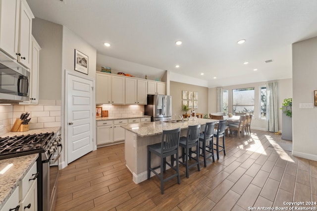 kitchen featuring light stone countertops, appliances with stainless steel finishes, light wood-type flooring, and a kitchen island with sink