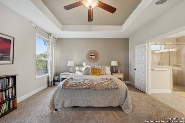 bedroom with a tray ceiling, ensuite bath, ceiling fan, and light carpet