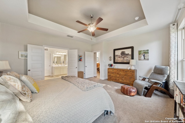 bedroom with ceiling fan, a raised ceiling, light colored carpet, and connected bathroom