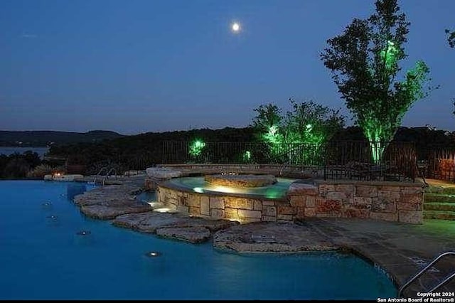 pool at dusk featuring an in ground hot tub and a patio area