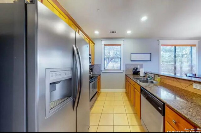 kitchen with dark stone counters, sink, light tile patterned floors, and stainless steel appliances