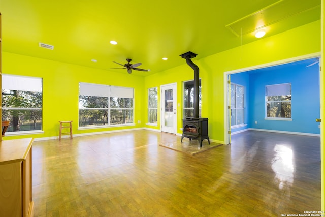 unfurnished living room with hardwood / wood-style flooring, a wood stove, and ceiling fan