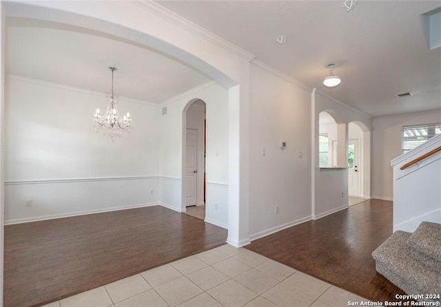 empty room featuring a notable chandelier, ornamental molding, and light hardwood / wood-style flooring