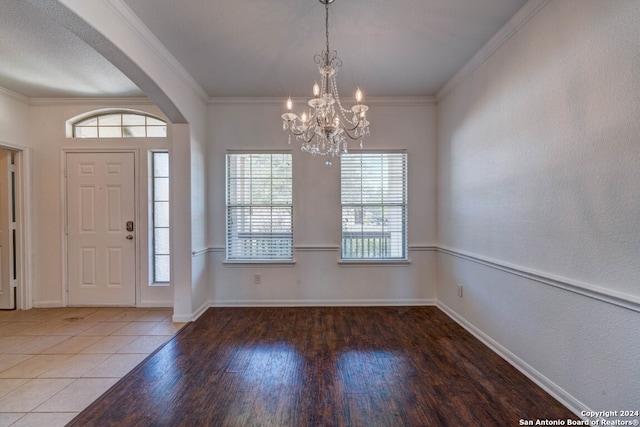 foyer with a notable chandelier, hardwood / wood-style floors, plenty of natural light, and ornamental molding