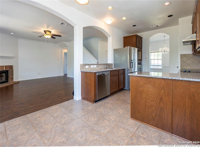 kitchen with light stone countertops, light hardwood / wood-style flooring, a fireplace, ceiling fan with notable chandelier, and appliances with stainless steel finishes