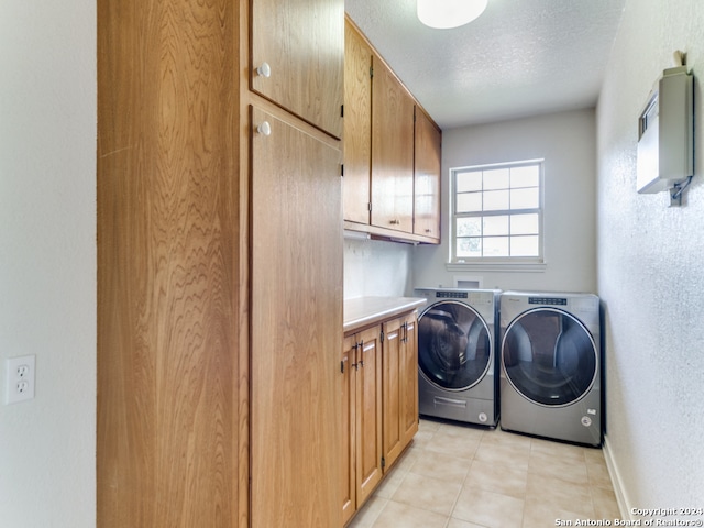 laundry area with washing machine and clothes dryer, light tile patterned floors, cabinets, and a textured ceiling