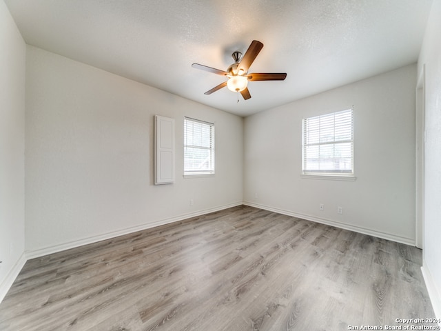 spare room with a textured ceiling, light wood-type flooring, ceiling fan, and a healthy amount of sunlight