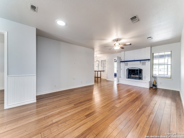 unfurnished living room featuring a textured ceiling, light hardwood / wood-style floors, a brick fireplace, and ceiling fan