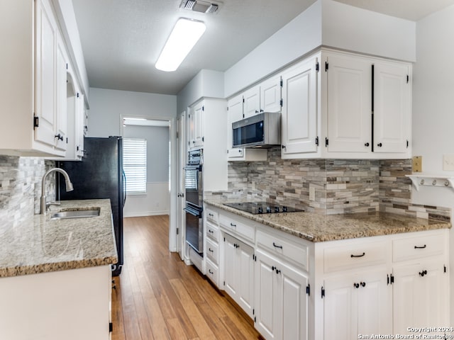 kitchen featuring white cabinets, appliances with stainless steel finishes, light hardwood / wood-style flooring, and light stone countertops