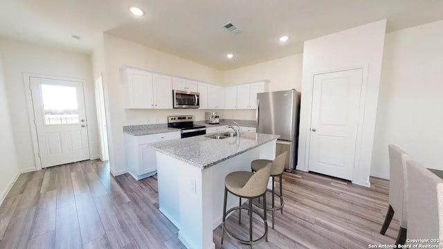 kitchen with white cabinets, stainless steel appliances, light hardwood / wood-style flooring, and a center island with sink