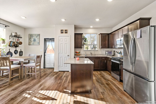 kitchen featuring appliances with stainless steel finishes, a kitchen island, dark brown cabinets, and dark wood-type flooring