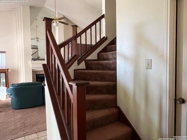 stairway featuring tile patterned floors, a tiled fireplace, and ceiling fan