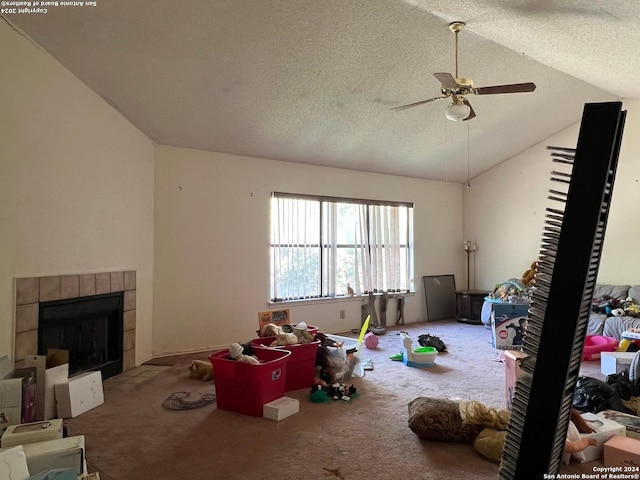 living room with carpet, a textured ceiling, ceiling fan, a tile fireplace, and lofted ceiling