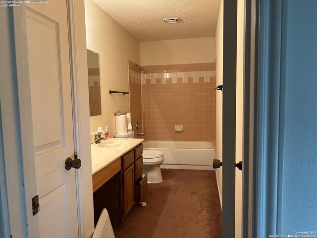 full bathroom with vanity, toilet, a textured ceiling, and tiled shower / bath