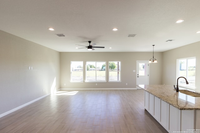 kitchen with light stone countertops, light wood-type flooring, sink, white cabinets, and hanging light fixtures