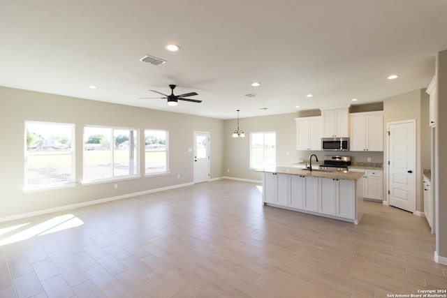 kitchen with a healthy amount of sunlight, white cabinetry, an island with sink, and appliances with stainless steel finishes