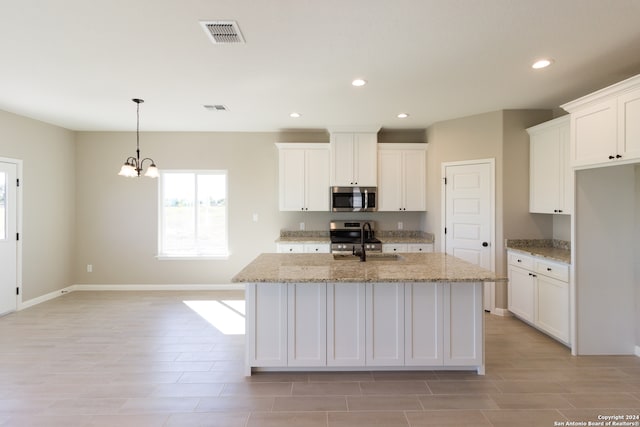 kitchen with light stone countertops, white cabinetry, a center island with sink, and stainless steel appliances