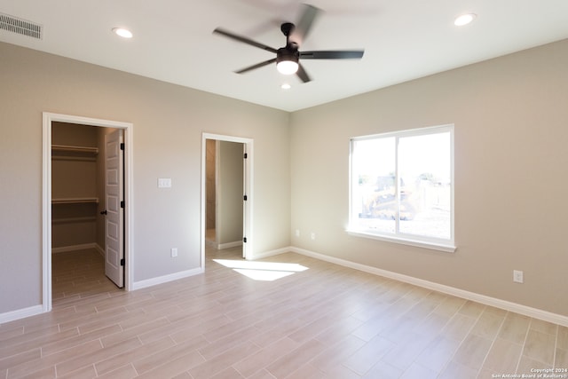 unfurnished bedroom with a walk in closet, ceiling fan, a closet, and light hardwood / wood-style floors