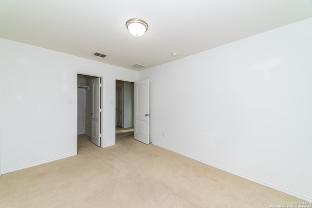 unfurnished bedroom with a walk in closet and light carpet