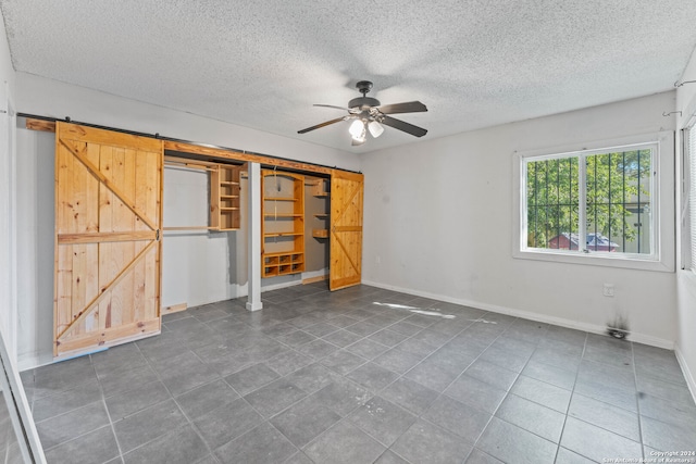 unfurnished bedroom featuring dark tile patterned flooring, ceiling fan, a barn door, a textured ceiling, and a closet