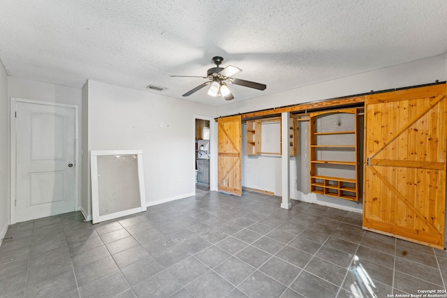 tiled empty room featuring ceiling fan, a barn door, and a textured ceiling