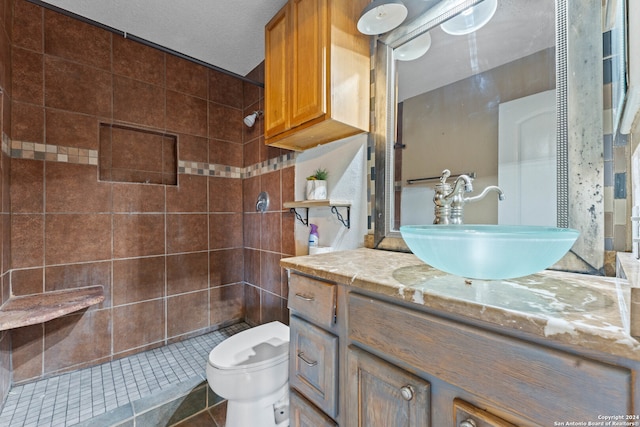 bathroom with vanity, tile patterned flooring, toilet, a textured ceiling, and a tile shower