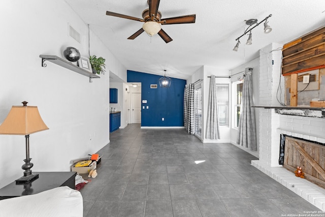 unfurnished living room featuring lofted ceiling, a brick fireplace, ceiling fan, dark tile patterned floors, and a textured ceiling