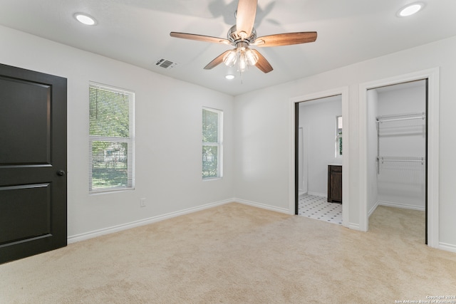 unfurnished bedroom featuring a walk in closet, light colored carpet, ceiling fan, and ensuite bathroom