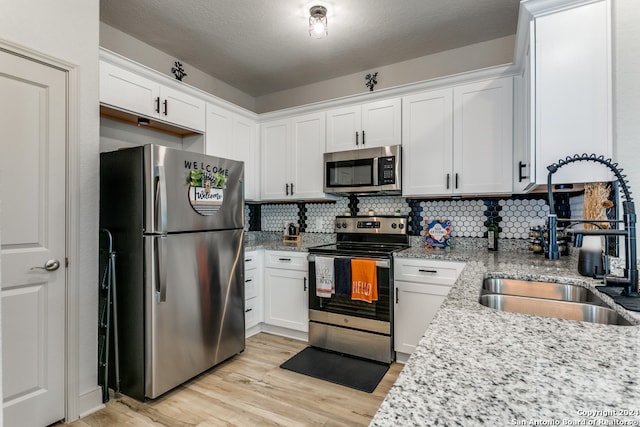 kitchen with sink, appliances with stainless steel finishes, tasteful backsplash, light stone counters, and white cabinetry