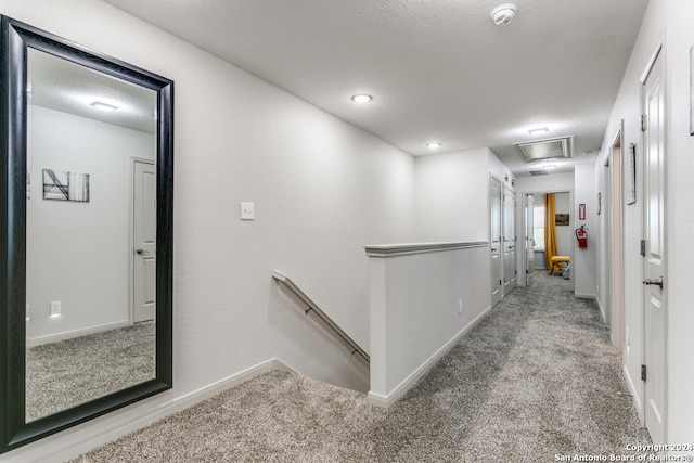 corridor with light colored carpet and a textured ceiling