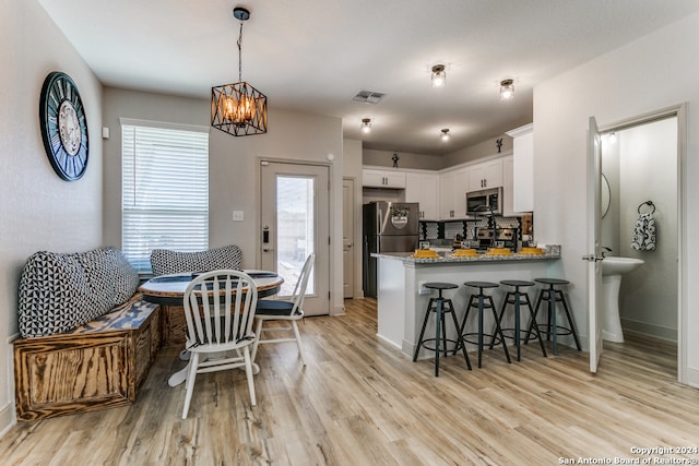 kitchen with pendant lighting, kitchen peninsula, appliances with stainless steel finishes, light stone counters, and white cabinetry