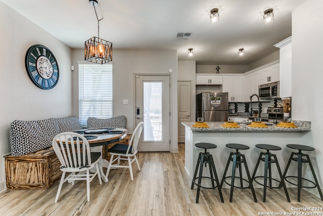 kitchen featuring light stone countertops, appliances with stainless steel finishes, kitchen peninsula, decorative light fixtures, and white cabinetry