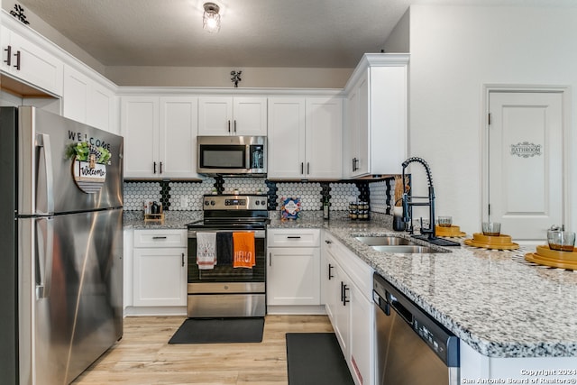 kitchen with light stone countertops, appliances with stainless steel finishes, backsplash, sink, and white cabinets