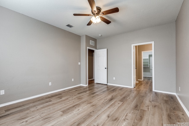 unfurnished bedroom featuring a walk in closet, a closet, light hardwood / wood-style flooring, and ceiling fan