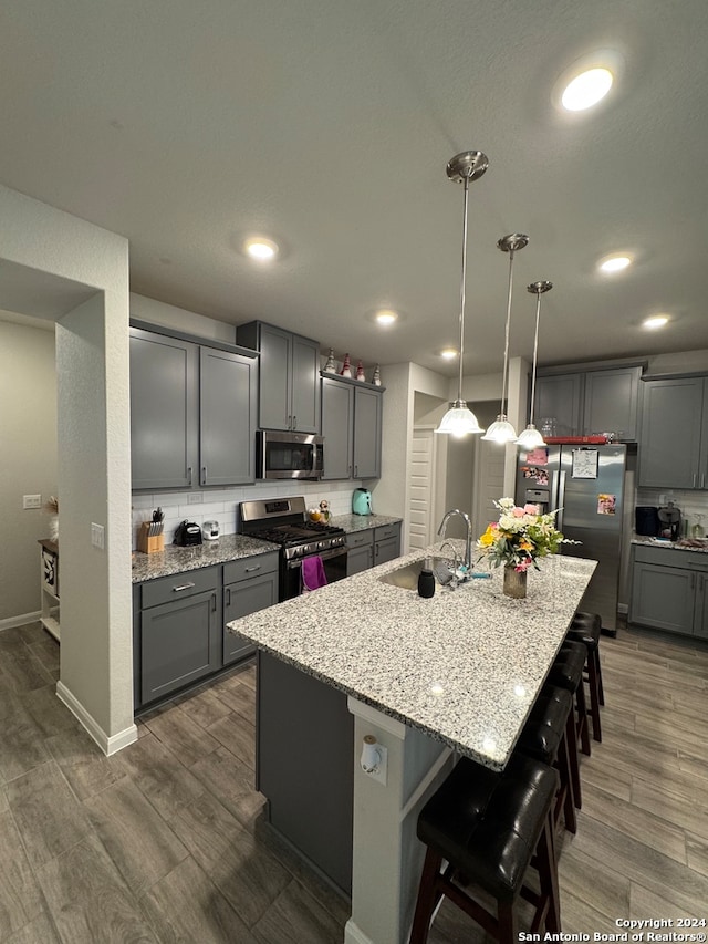 kitchen featuring appliances with stainless steel finishes, sink, a center island with sink, decorative light fixtures, and gray cabinets