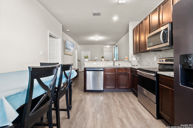 kitchen featuring kitchen peninsula, decorative backsplash, stainless steel appliances, sink, and light hardwood / wood-style floors