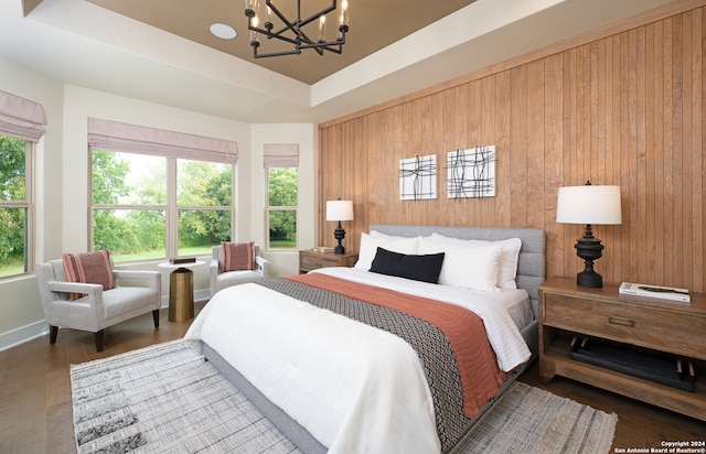 bedroom with a tray ceiling, wooden walls, dark hardwood / wood-style flooring, and a chandelier