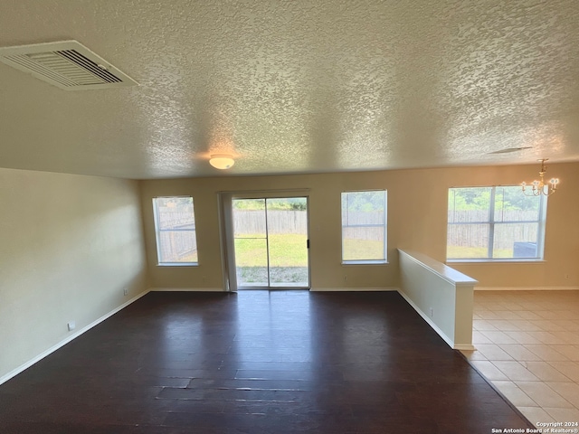 unfurnished room featuring a notable chandelier, a healthy amount of sunlight, dark hardwood / wood-style flooring, and a textured ceiling