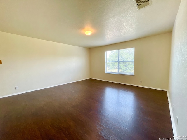 spare room with a textured ceiling and dark hardwood / wood-style floors